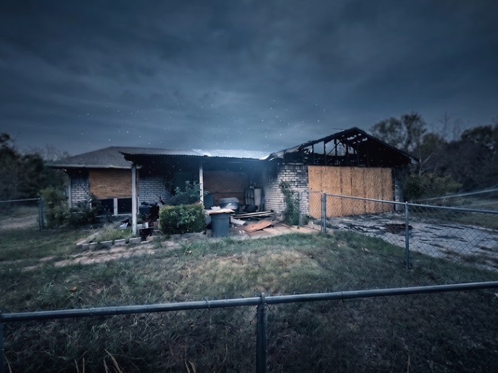 Fire-damaged house with boarded windows and a burned-out roof at dusk in Dallas-Fort Worth